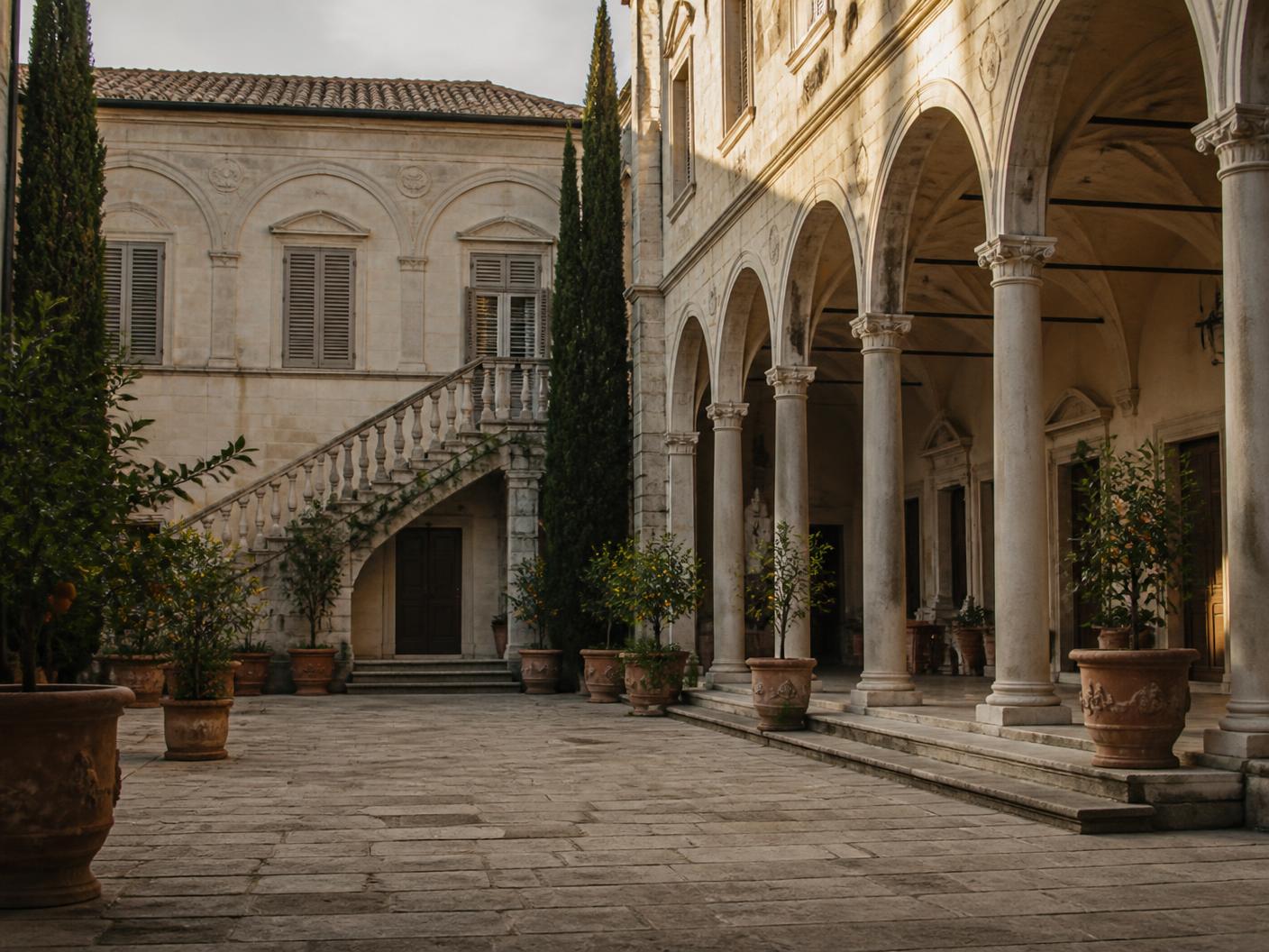 The stone courtyard and arcaded loggia of a maintained historic palazzo in late afternoon light.